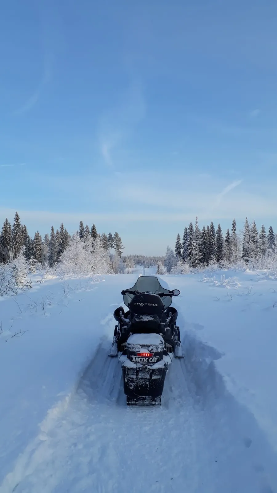 Deux personnes sur une motoneige traversant un lac gelé bordé de forêt givrée